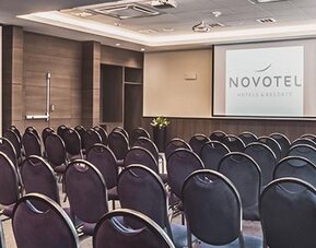 Conference room arranged with rows of chairs facing a presentation screen and a front table at Novotel Lima San Isidro.
