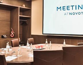 Private meeting room with a round conference table, upholstered chairs, water bottles and a presentation screen at Novotel Lima San Isidro.