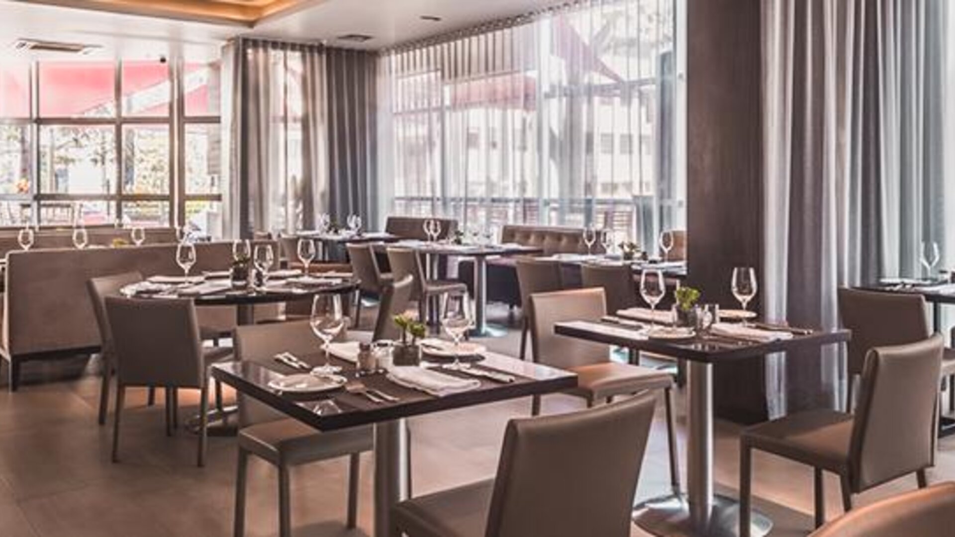 Hotel restaurant with neatly arranged dining tables, upholstered chairs, floor-to-ceiling windows and curtains at Novotel Lima San Isidro.