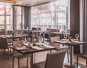 Hotel restaurant with neatly arranged dining tables, upholstered chairs, floor-to-ceiling windows and curtains at Novotel Lima San Isidro.