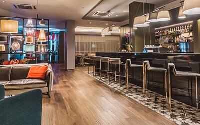 Hotel bar with dark leather sofas, colorful accent cushions, upholstered chairs, high stools and illuminated shelving at Novotel Lima San Isidro.