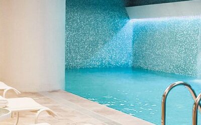 Indoor swimming pool with turquoise water, mosaic-tiled walls and white loungers along the poolside at Novotel Lima San Isidro.