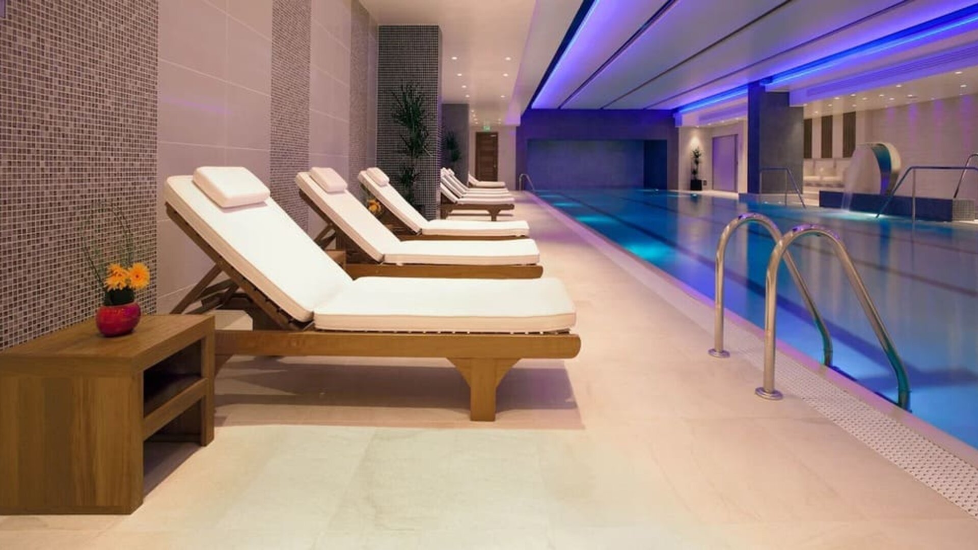 Relaxing indoor heated pool with comfortable lounge chairs at Leonardo Royal Hotel London Tower Bridge.