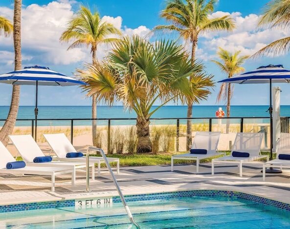 Refreshing outdoor pool surrounded by sun loungers with a view of the ocean at Plunge Beach Resort.
