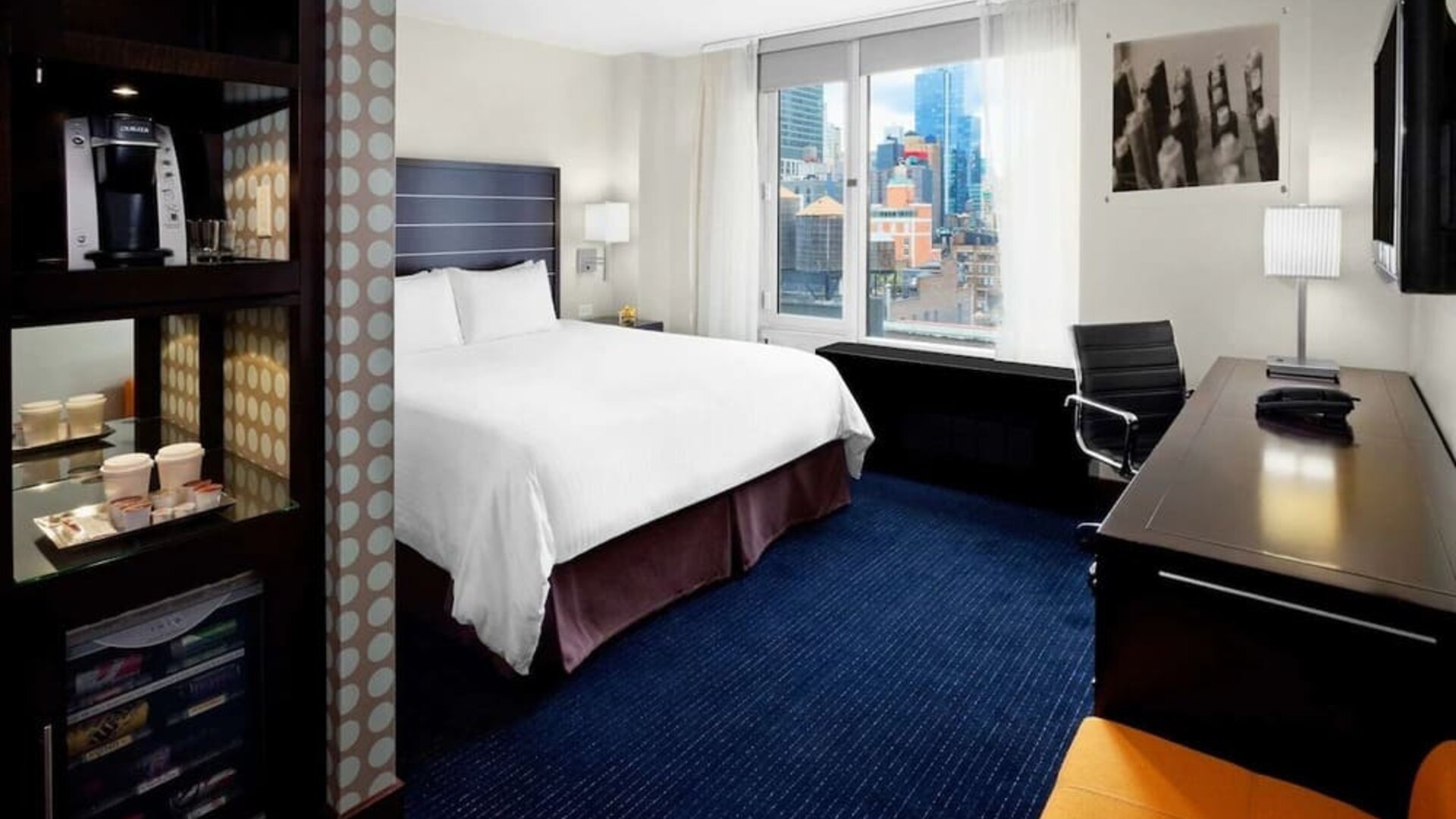 King bedroom with TV, work station and a view of the city at Hilton New York Fashion District.