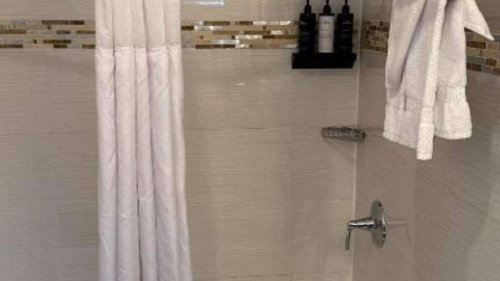 Bathroom at Madison LES Hotel with bathtub and shower with privacy curtains and towels.