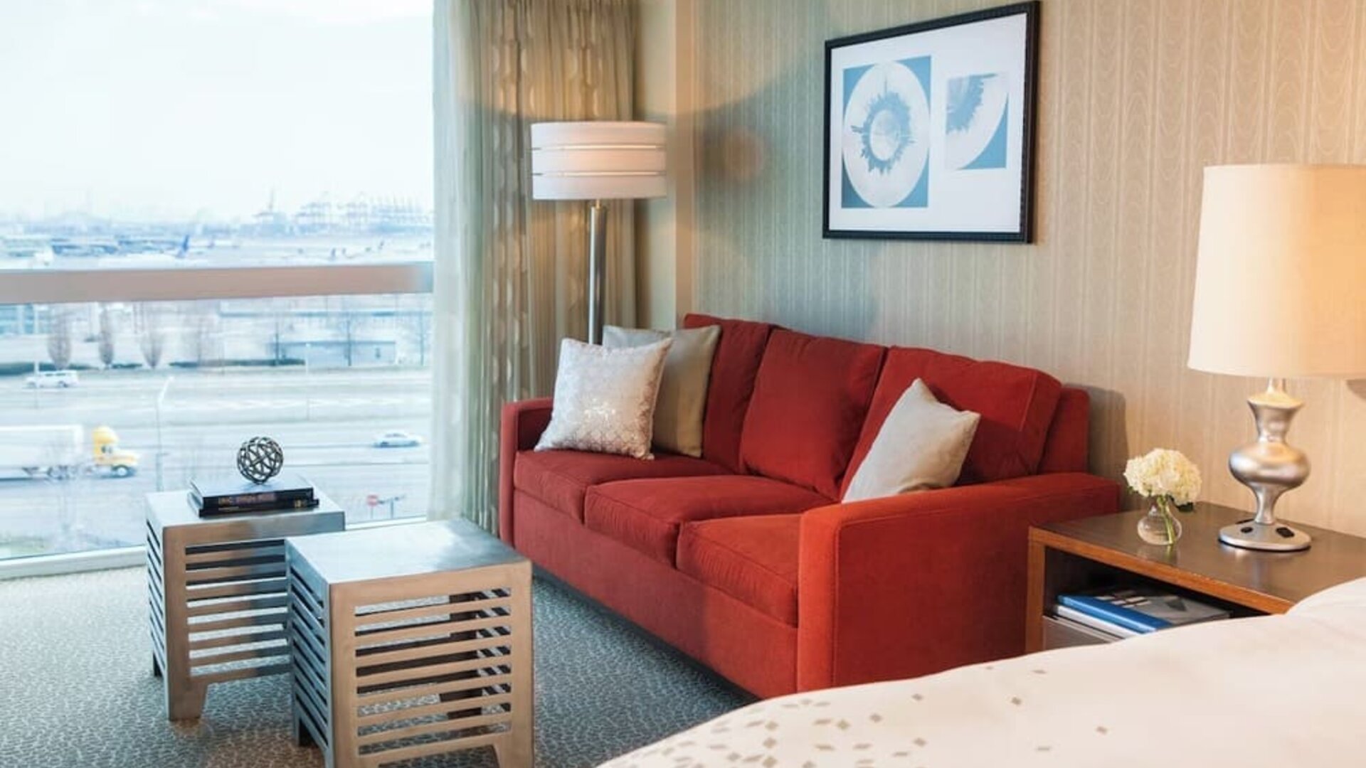 Guest room seating area with red sofa, coffee table, large window view, and bedside lamp at Renaissance Newark Airport Hotel.