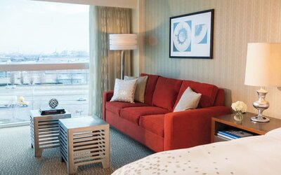 Guest room seating area with red sofa, coffee table, large window view, and bedside lamp at Renaissance Newark Airport Hotel.