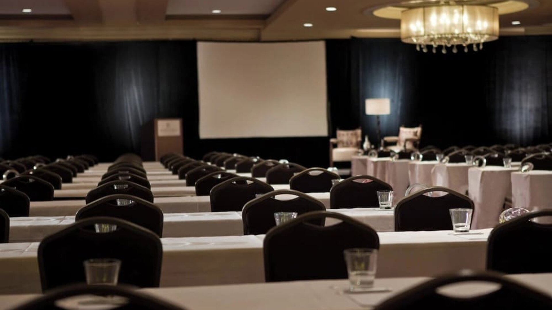 Conference room with rows of tables and chairs facing projector screen and podium at Renaissance Newark Airport Hotel.