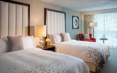 Guest room with two beds, bedside table, lamp, armchair, and window with curtains at Renaissance Newark Airport Hotel.