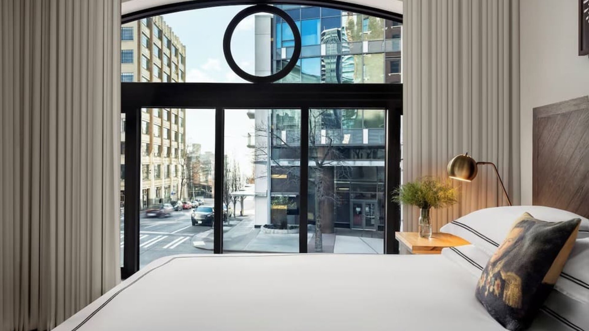 Bedroom with large window showing city street view, white bedding, and neutral decor at Kimpton Palladian Hotel.