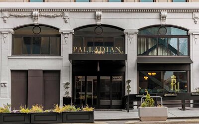 Hotel entrance with black awning, signage, and planters along sidewalk at Kimpton Palladian Hotel.