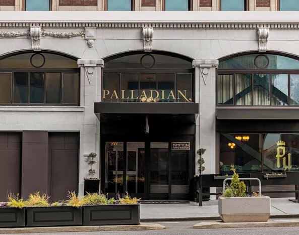 Hotel entrance with black awning, signage, and planters along sidewalk at Kimpton Palladian Hotel.
