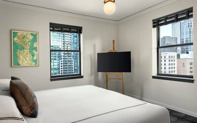 Bedroom with king bed, two windows showing city buildings, and television on stand at Kimpton Palladian Hotel.