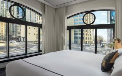 Corner bedroom with large curved windows, city street views, and white bedding at Kimpton Palladian Hotel.