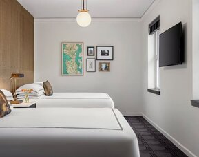 Guest room with two beds, city view windows, and wall-mounted TV in bright interior at Kimpton Palladian Hotel.