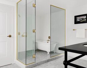 Bathroom with glass shower, freestanding clawfoot tub, white tile walls, and brass fixtures at Kimpton Palladian Hotel.