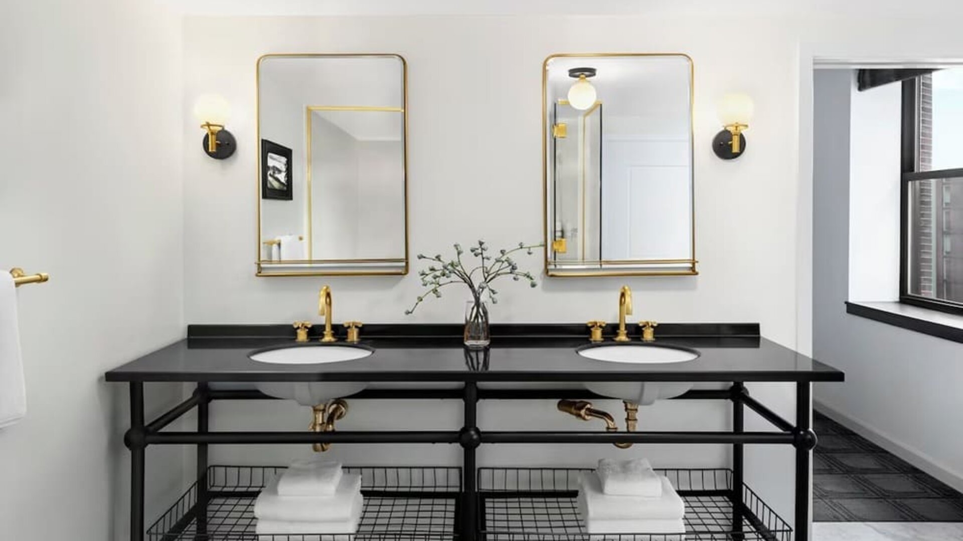 Double vanity bathroom with black countertop, gold fixtures, twin mirrors, and towels at Kimpton Palladian Hotel.