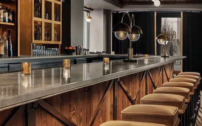 Long marble bar counter with upholstered stools, pendant lighting, and liquor shelves at Kimpton Palladian Hotel.