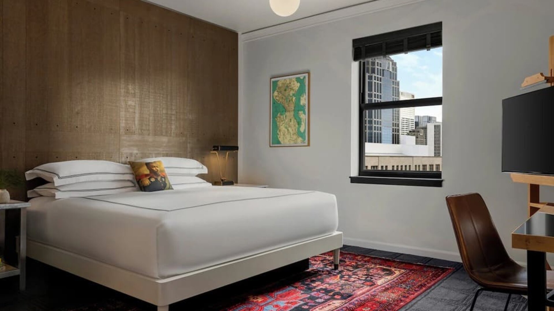 Guest room with king bed, wood accent wall, desk, chair, and patterned rug at Kimpton Palladian Hotel.