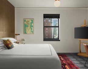 Bright bedroom with king bed, dual windows with city buildings, and framed artwork at Kimpton Palladian Hotel.