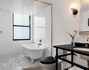Bathroom with freestanding tub, glass partition, black vanity, and gold fixtures at Kimpton Palladian Hotel.