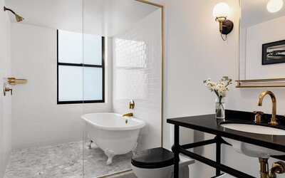 Bathroom with freestanding tub, glass partition, black vanity, and gold fixtures at Kimpton Palladian Hotel.