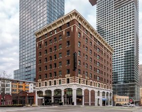 Exterior of multi-story brick building on city corner with surrounding towers at Kimpton Palladian Hotel.