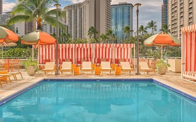 Outdoor pool with lounge chairs, umbrellas, and surrounding city buildings at The Ambassador Hotel Of Waikiki.