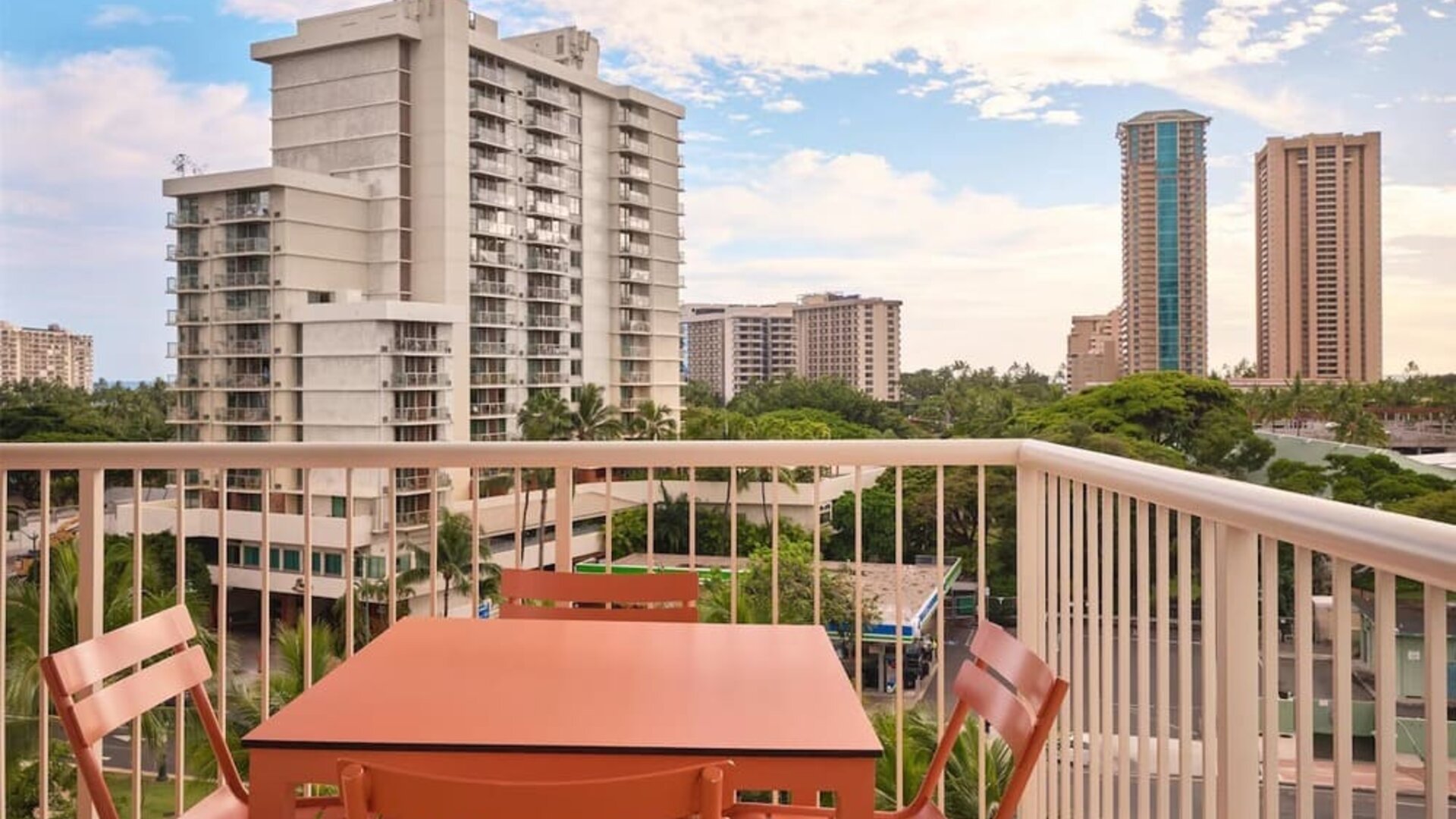 Balcony with table and chairs overlooking city buildings and palm trees at The Ambassador Hotel Of Waikiki.