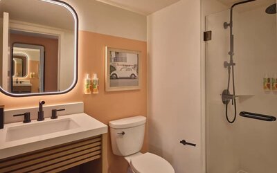 Modern bathroom with walk-in shower, illuminated mirror, and vanity at The Ambassador Hotel Of Waikiki.