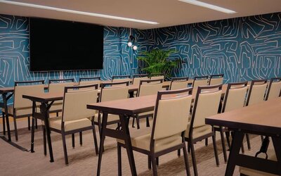Conference room with rows of tables, chairs, and wall-mounted screen at The Ambassador Hotel Of Waikiki.