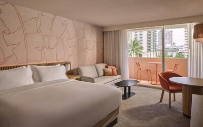 Guest room with bed, sofa seating area, and balcony access with city view at The Ambassador Hotel Of Waikiki.