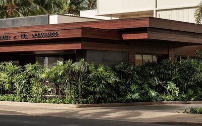 Exterior view of hotel entrance with tropical landscaping and signage at The Ambassador Hotel Of Waikiki.