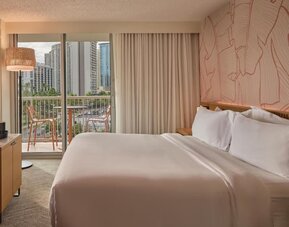 Guest room with king bed, balcony, and city skyline view at The Ambassador Hotel Of Waikiki.