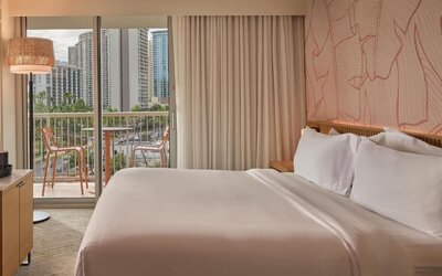 Guest room with king bed, balcony, and city skyline view at The Ambassador Hotel Of Waikiki.