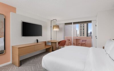 Guest room with balcony, seating area, and TV console at The Ambassador Hotel Of Waikiki.