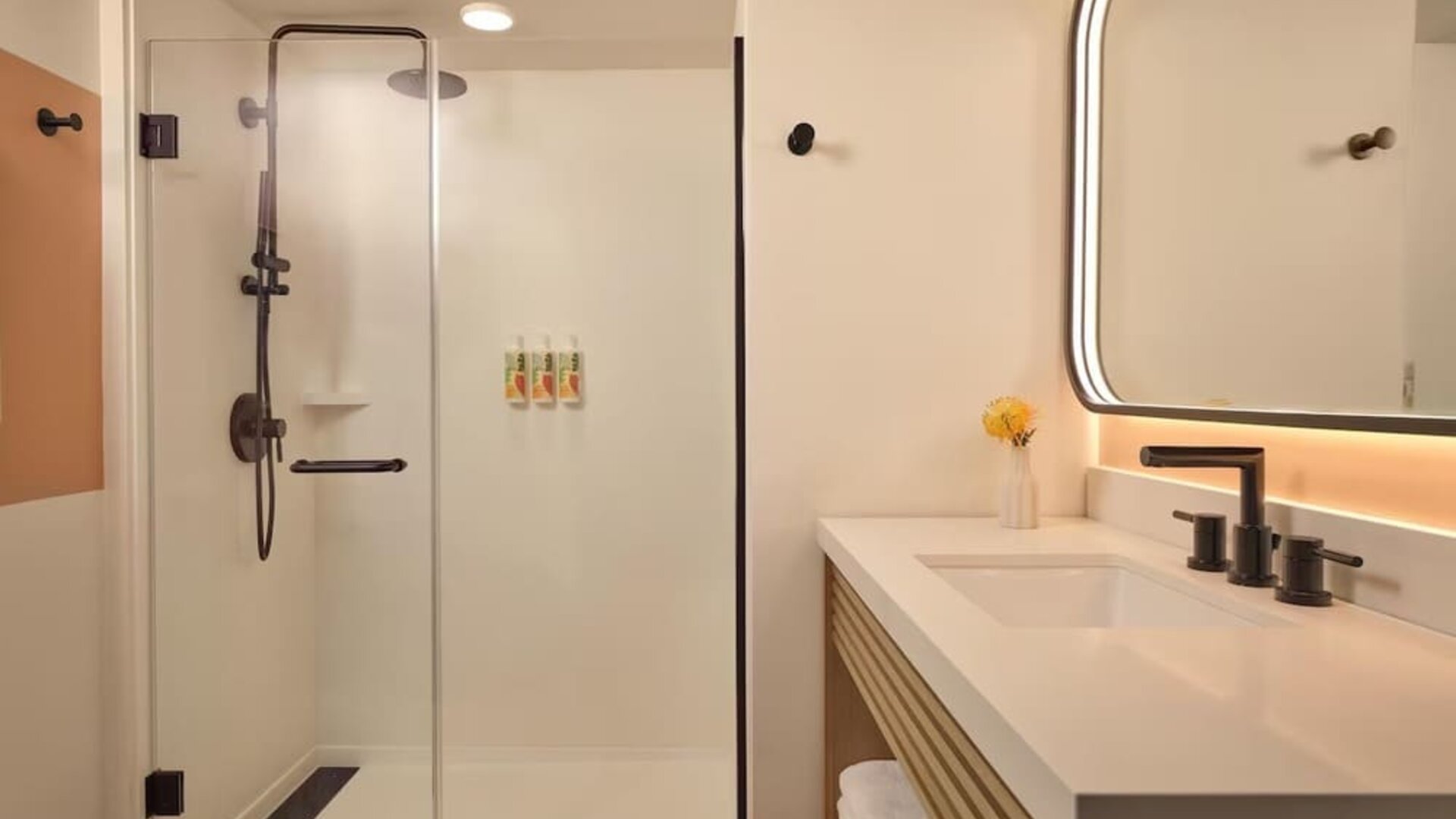 Modern bathroom with walk-in glass shower, vanity, and illuminated mirror at The Ambassador Hotel Of Waikiki.