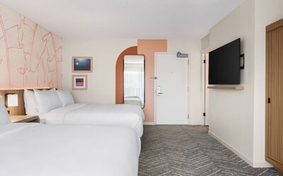 Guest room with two beds, wall-mounted TV, and minimalist decor at The Ambassador Hotel Of Waikiki.