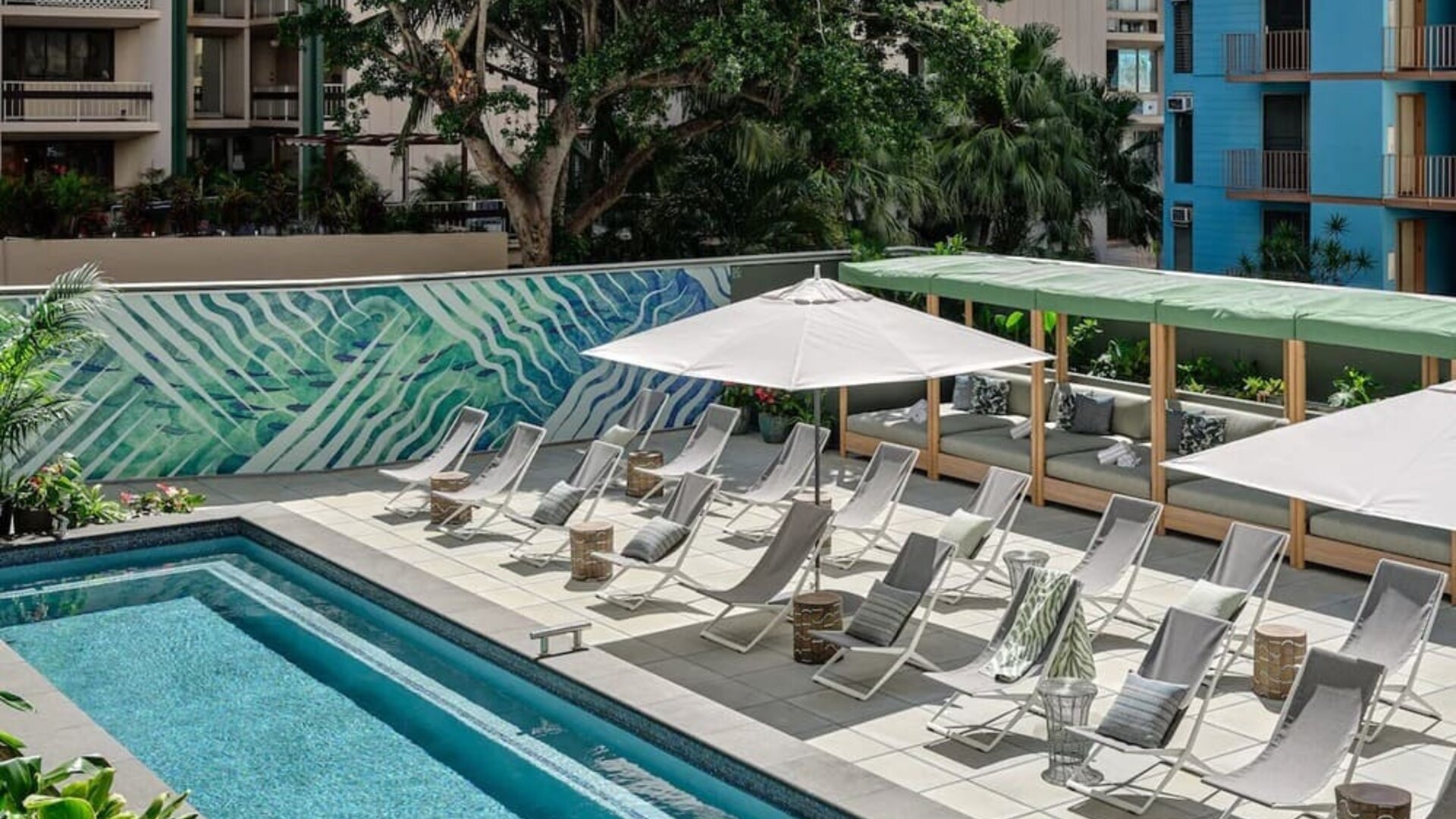 Poolside area with loungers, umbrellas, shaded seating, and bar visible in the background at Romer House Waikiki.