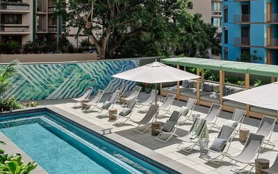 Poolside area with loungers, umbrellas, shaded seating, and bar visible in the background at Romer House Waikiki.
