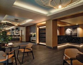 Reception lounge with warm lighting, wooden finishes, seating areas, and decorative ceiling fixtures at Romer House Waikiki
