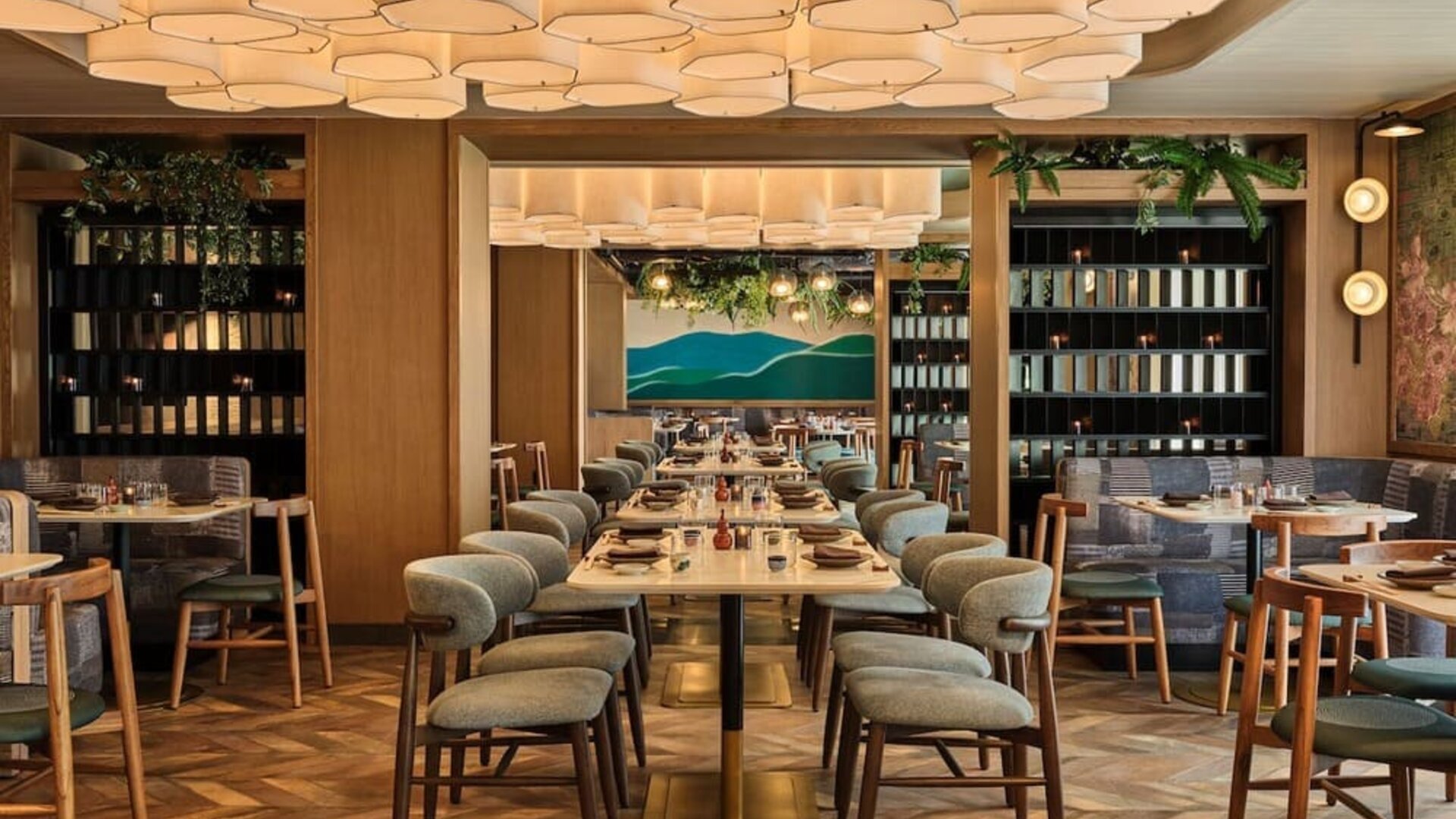 Restaurant dining space with long tables, cushioned chairs, wood accents, and decorative ceiling lighting at Romer House Waikiki.