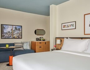 Blue sofa, round table, wooden cabinet, and wall art in a relaxed guest room at Romer House Waikiki.