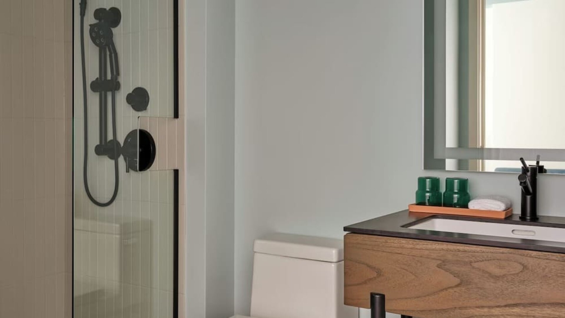 Compact bathroom with glass shower, modern vanity, mirror, and neatly folded towels below sink at Romer House Waikiki.