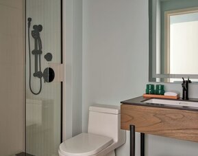 Compact bathroom with glass shower, modern vanity, mirror, and neatly folded towels below sink at Romer House Waikiki.