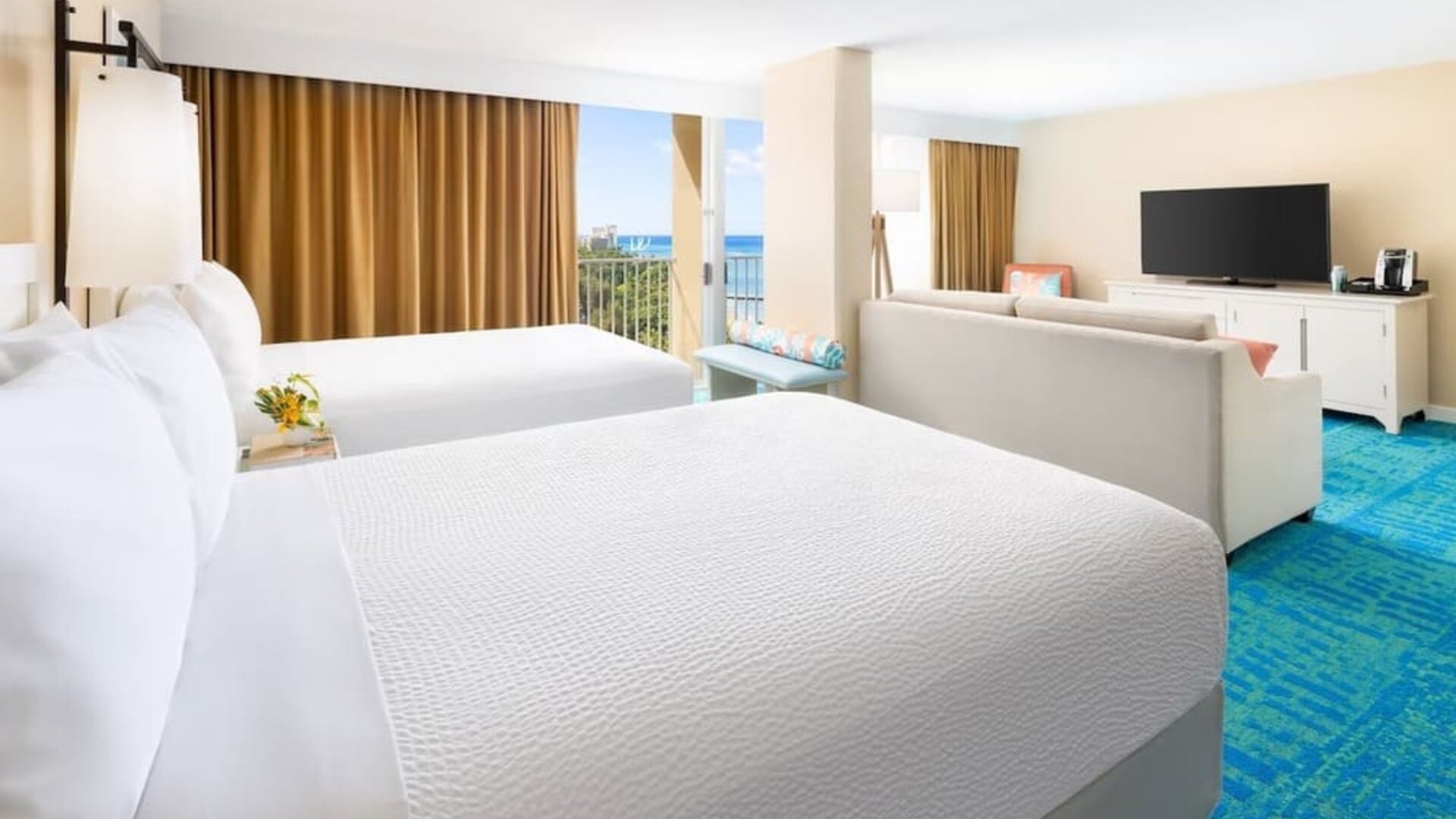 Two double beds with balcony view, seating area, and partial ocean glimpse at The Twin Fin Hotel.