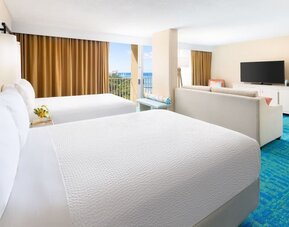 Two double beds with balcony view, seating area, and partial ocean glimpse at The Twin Fin Hotel.