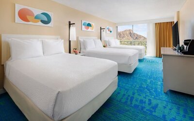 Room with three double beds, balcony view, and mountain backdrop at The Twin Fin Hotel.