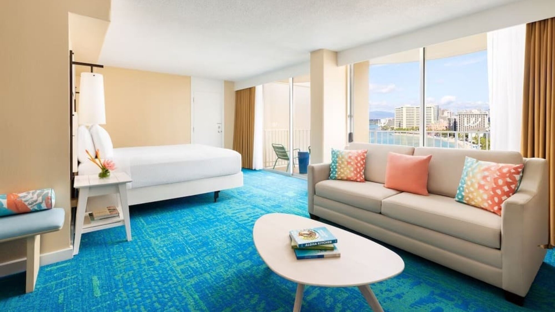 Bright suite with king bed, sofa seating area, colorful pillows, and ocean-facing balcony at The Twin Fin Hotel.